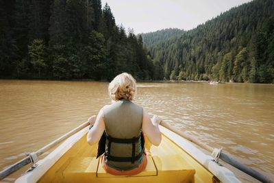 Rear view of woman rowing boat in river against mountains