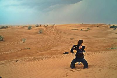Rear view of young woman sitting on tire at desert