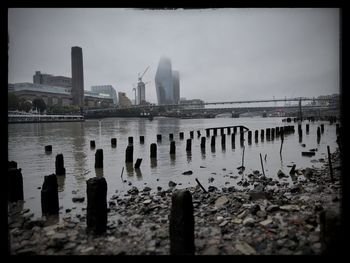 Wooden posts in river against buildings in city