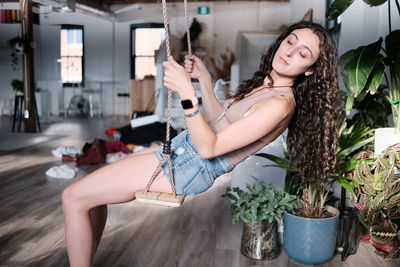 Beautiful woman sitting on an indoor wooden swing, surrounded by plants and in bliss 