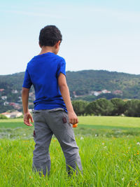 Rear view of kid standing on field against sky