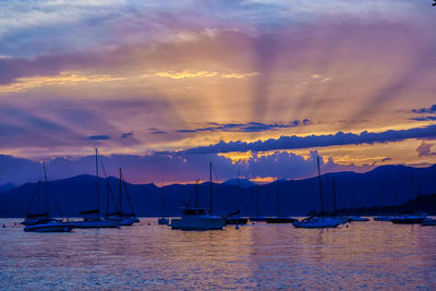 Sailboats moored on harbor against sky during sunset