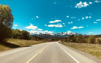 Empty road by trees against sky