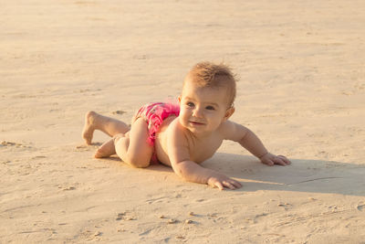 Little baby girl is crawling on a sandy beach near to sea in sunset sunlight.