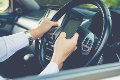 Businessman touching and using smartphone for online chat in front of steering wheel at front seat 
