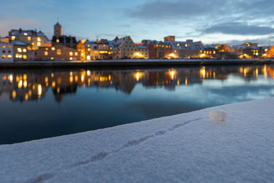 River by illuminated city against sky at dusk