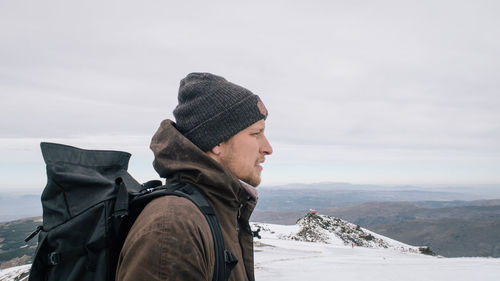 Male hiker standing on snow covered mountain against sky