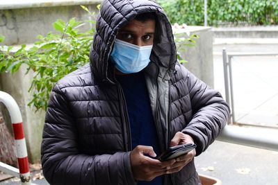 Portrait of man wearing mask using mobile phone standing outdoors