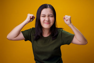 Portrait of young woman standing against yellow background