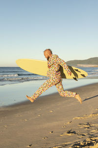 Carefree man running with surfboard on beach