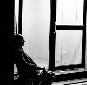 Side view of man sitting on window