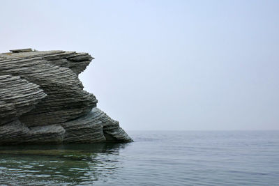 Rock formation in sea against clear sky