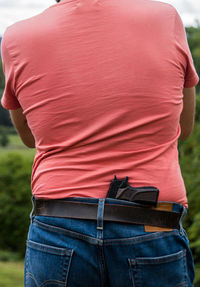 Rear view of man standing outdoors with a gun