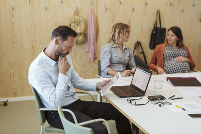 Mature professional using digital tablet while sitting with colleagues in meeting