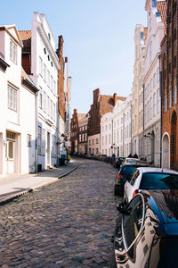 Vehicles parked on cobbled street amidst buildings in city