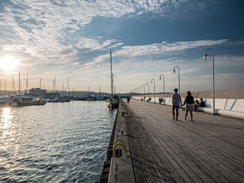 People on pier at sea against sky