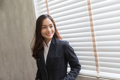 Portrait of smiling young woman standing against wall