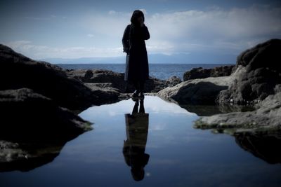 Woman with reflection standing at calm sea