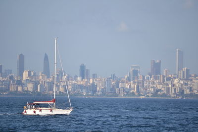 Sailboats sailing on sea against buildings in city