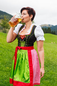 Mid adult woman drinking beer while standing on grassy field