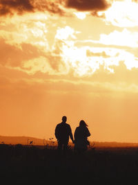 Silhouette couple standing on field against sky during sunset