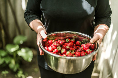 Midsection of woman holding strawberries in bowl