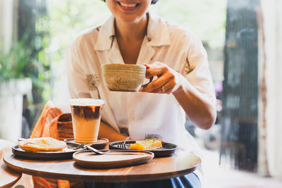 Happy woman drinks coffee and eats cake in cafe.