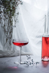 Glass of red drink on white backlight window background with bottle