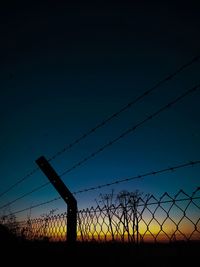 Silhouette barbed wire on field against clear sky at sunset