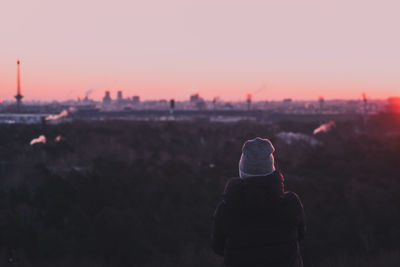 Rear view of woman standing against sky during sunset