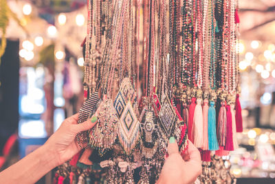 Cropped hands of woman holding multi colored necklaces for sale in store