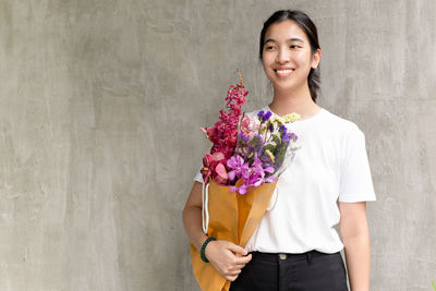 Cheerful woman holding bouquet standing against wall