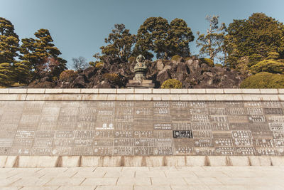 Text on wall by trees against sky