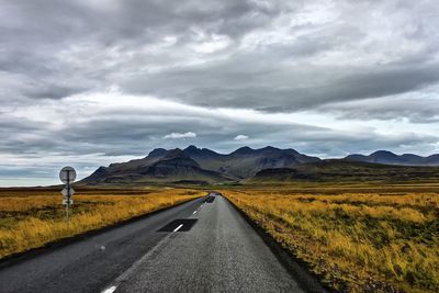 Road passing through landscape against dramatic sky