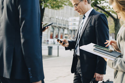 Business professionals using smart phone while standing in city