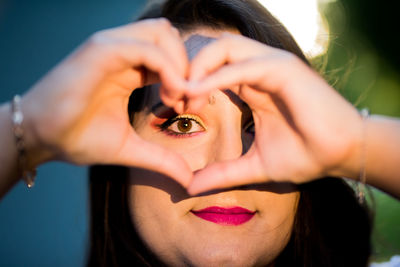 Close-up portrait of young woman looking through heart shape