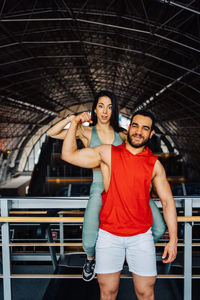 Portrait of young woman standing in gym holding muscles and cheering 