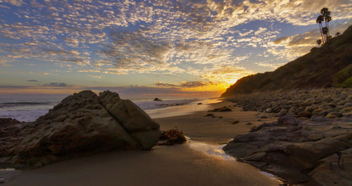 Rocks on beach against sky during sunset