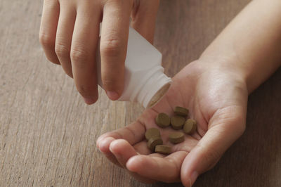 Cropped hands of person holding medicine bottle on wooden table