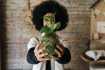 Portrait of man holding plant against wall