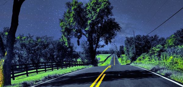 Road amidst trees against clear sky at night