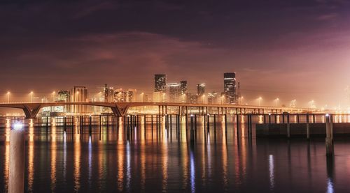 Illuminated bridge over sea against sky at night