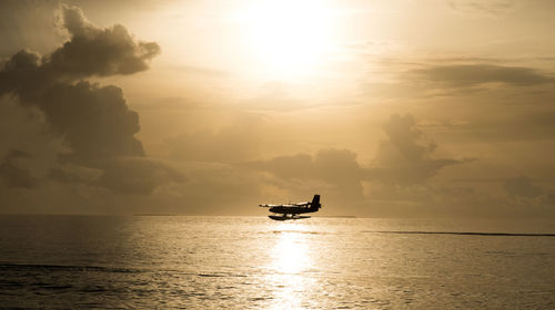 Silhouette air vehicle flying over sea against sky during sunset