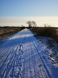 Snow covered road amidst field against sky