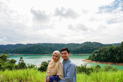 Portrait of young couple by lake against sky