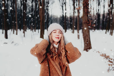 Photo of young beautiful woman in fur coat standing on the white snow in winter forest. girl smiling