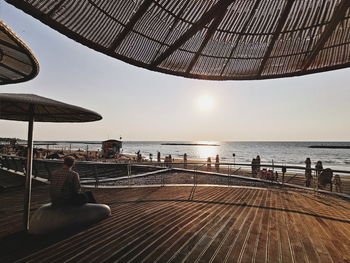 People sitting by sea against sky during sunset