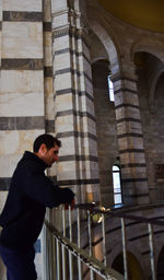 Side view of young man standing against building