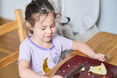 Young girl eating eggs and bacon with knife and fork for the first time