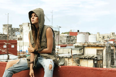 Portrait of young woman sitting against buildings